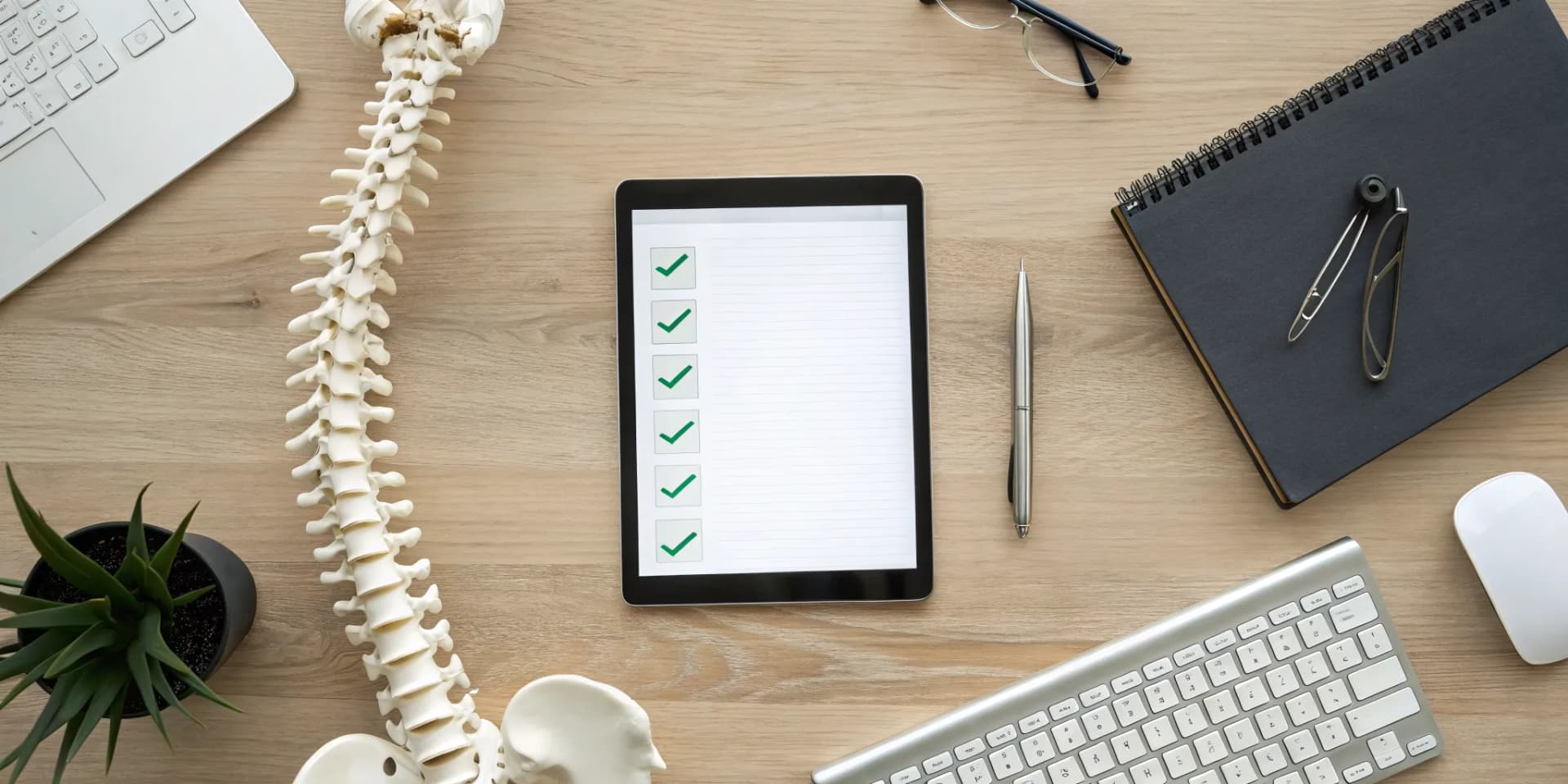 Chiropractic practice purchase checklist on a tablet, next to a model of a spine.